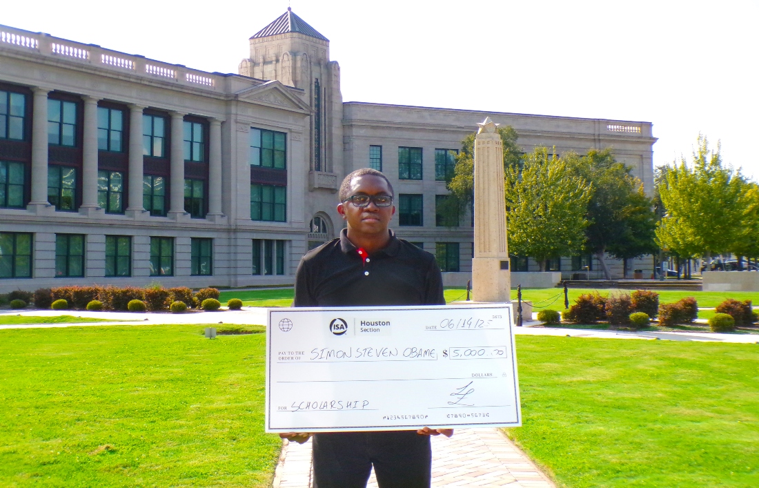 Simon Obame stands in front of the HCC Central Campus holding a scholarship check from the International Society of Automation, Houston Section.